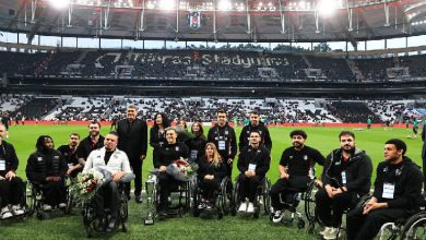 Görselde, bir futbol stadyumunun çim sahasında bir araya gelmiş büyük bir grup görülüyor. Ön sırada tekerlekli sandalyede bulunan sporcular yer alırken, arkalarında teknik ekip ve yöneticiler ayakta duruyor. Sporcuların çoğunun elinde kupa ve çiçek buketleri bulunuyor. Arka planda tribünlerde “Tüpraş Stadyumu” yazısı seçiliyor. Atmosfer, bir kutlama ve onurlandırma töreni havası taşıyor.