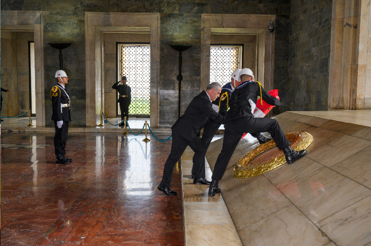 Anıtkabir’in iç bölümünde gerçekleştirilen resmi törende bir kişi, askerlerin yardımıyla mozoleye çelenk bırakıyor. Törende nöbet tutan askerler resmi üniformalarıyla yer alırken, ortam saygı ve anma atmosferi taşıyor.