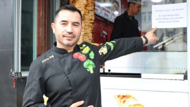 Önünde “İkramda Engel Yok” yazan afişi gösteren bir aşçı ve arka planda döner tezgâhı.