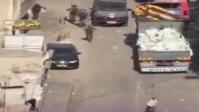 Yüksekten çekilmiş bir sokak görüntüsünde, araçların bulunduğu dar bir yolda birkaç kişi koşuşturuyor. Bir kamyon ve otomobiller yol üzerinde dururken, çevrede dağınık eşyalar dikkat çekiyor. Sahne, ani gelişen bir olay ya da gerginlik anını andırıyor.