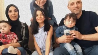 Altı kişilik, samimi bir aile pozu; yetişkinler ve çocuklar koltuk etrafında yakın şekilde oturuyor.