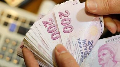Bir kişinin elinde deste hâlinde 200 TL banknotlar var; arka planda bulanık bir hesap makinesi görülüyor.