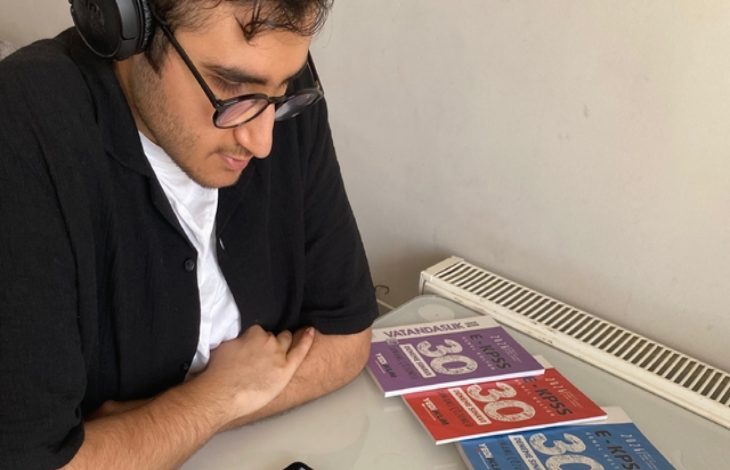 Görme engelli Ömer Miraç Şahin sırada oturuyor ve önünde üç tane EKPSS kitapçığı bulunuyor.