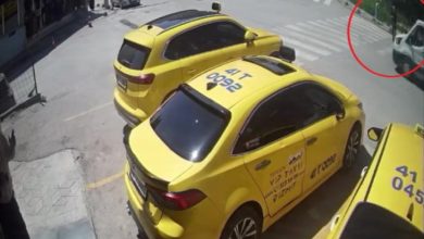 Güvenlik kamerası görüntüsünde sarı taksi ve yolun karşısında görme engelli birey, yaya geçidinde geçiyor.