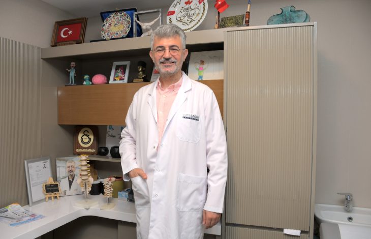 Özel Sağlık Hastanesi Beyin ve Sinir Cerrahisi Uzmanı Op. Dr. Serkan Zengin, çalışma odasında ayakta durmakta ve gülümsemektedir.