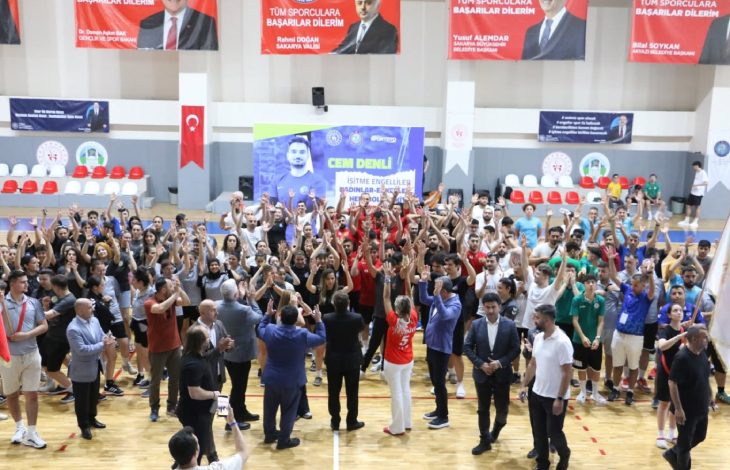 Bu görselde, bir spor salonunda düzenlenen kalabalık bir etkinlik sırasında katılımcılar ellerini havaya kaldırarak coşkulu bir şekilde kutlama yaparken, salonun ortasında bulunan görevliler ve sporcular etkinliğe eşlik etmektedir.