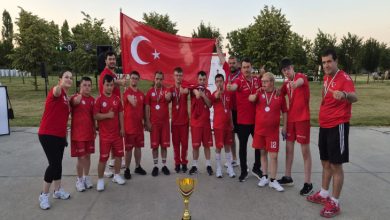 Görselde, kırmızı milli takım formaları giyen sporcular ve teknik ekip, ellerindeki madalyalarla Türk bayrağı önünde toplu fotoğraf veriyor. Ön planda kupa yer alırken, takımın şampiyona sonrası elde ettiği dereceyi birlikte kutladığı gururlu ve coşkulu bir an yansıtılıyor.