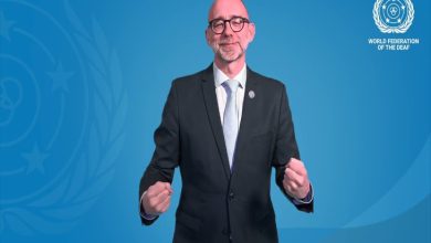 Mavi arka plan önünde takım elbiseli ve gözlüklü bir kişi, el hareketleriyle işaret dili kullanırken görülüyor. Görselde Dünya Sağırlar Federasyonu (WFD) logosu ve “World Congress” yazısı yer alıyor.