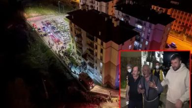 Görsel, gece saatlerinde meydana gelen bir olaya ilişkin haber fotoğrafı niteliğinde. Fotoğrafın ana bölümünde çok katlı bir apartmanın çevresi havadan görüntülenmiş; bina önünde itfaiye ve acil durum araçları ile toplanan kalabalık dikkat çekiyor. Bölge kırmızı ve mavi acil durum ışıklarıyla aydınlatılmış durumda. Sağ alt köşedeki ek karede ise iki kişinin destek verdiği yaşlı bir erkek görülüyor. Yaşlı kişinin üzgün ve endişeli bir ifade taşıdığı, çevresinde maske takan görevlilerin bulunduğu seçiliyor. Görsel genel olarak bir yangın veya acil müdahale sonrası yaşanan gelişmeleri yansıtan haber fotoğrafı izlenimi veriyor.