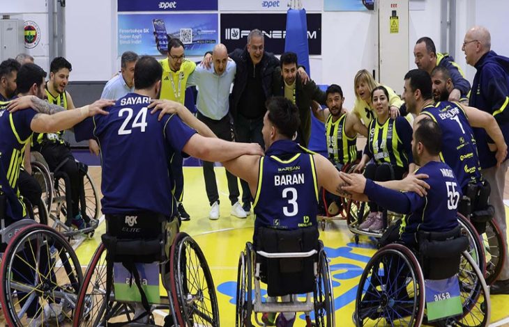 Fenerbahçe İstanbul Jet Tekerlekli Sandalye Basketbol Takımı oyuncuları ve teknik ekibi, çember oluşturup omuz omuza vererek takım ruhunu yansıtan coşkulu bir an yaşamaktadır.