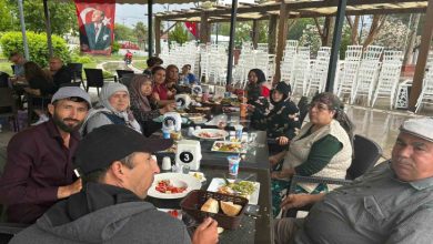 Görselde, açık alanda düzenlenen bir etkinlikte uzun bir masa etrafında bir araya gelen aileler yemek eşliğinde vakit geçiriyor. Türk bayrakları ve doğayla iç içe ortam dikkat çekerken, katılımcıların birlikte zaman geçirdiği samimi ve sosyal bir buluşma atmosferi öne çıkıyor.