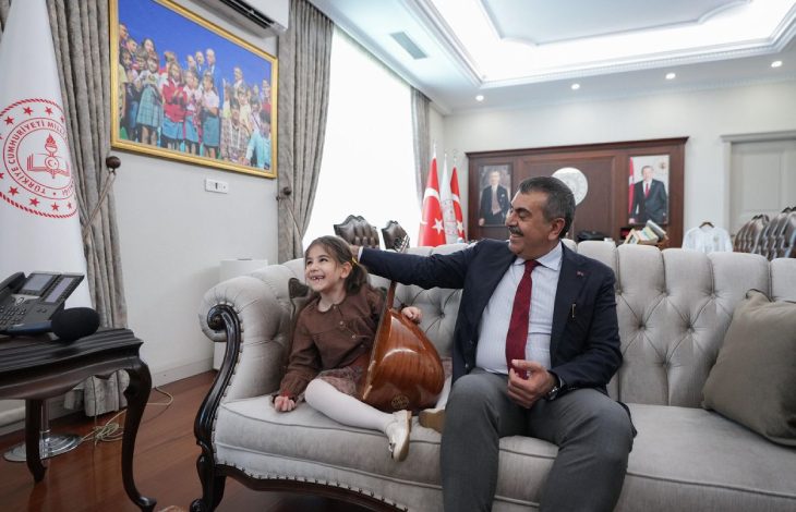 Görme engelli Nil Korkmaz bağlama tutarak Milli Eğitim Bakanı Yusuf Tekin ile koltukta oturuyor.