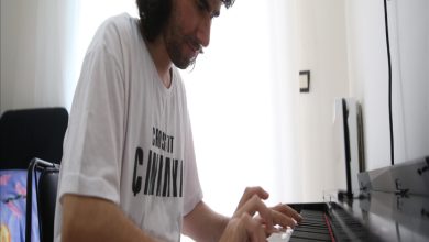 Bir kişi, aydınlık bir odada dijital piyano çalıyor. Beyaz tişört giymiş ve tuşlara odaklanmış halde oturuyor; ortam sakin ve müzik çalışması havası veriyor.
