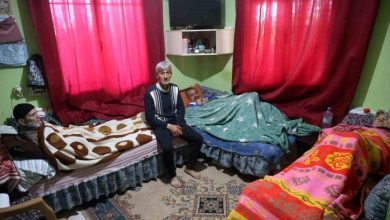 Görselde, mütevazı bir ev ortamında aynı odada kalan yaşlı bireyler ve ortada oturan bir kişi görülüyor. Yatakların yan yana yer aldığı odada bakım ve birlikte yaşam düzeni dikkat çekerken, sahne aile içi dayanışma, sorumluluk ve uzun süreli bakımın günlük yaşamını yansıtıyor.