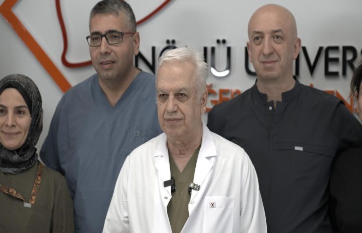 Görselde, bir sağlık kuruluşunda çekilmiş toplu bir fotoğraf yer alıyor. Ön sırada beyaz önlük giyen yaşlı bir doktor bulunurken, arkasında ve yanında sağlık çalışanları görülüyor. Arka planda hastane veya tıp merkezi logosunun bir bölümü yer alıyor. Fotoğraftaki kişiler kameraya dönük şekilde poz veriyor ve görüntü, tıbbi bir başarı ya da basın açıklaması sonrası çekilmiş ekip fotoğrafı izlenimi veriyor.