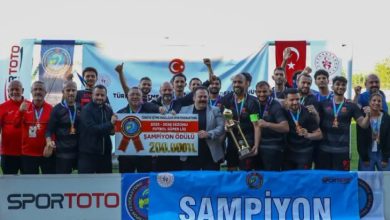Şampiyonluk kupasını ve ödül çekini birlikte kaldıran madalyalı futbolcular ile teknik ekip, 'Şampiyon' yazılı pankart önünde sevinçle poz vererek elde ettikleri başarıyı kutlamakta.