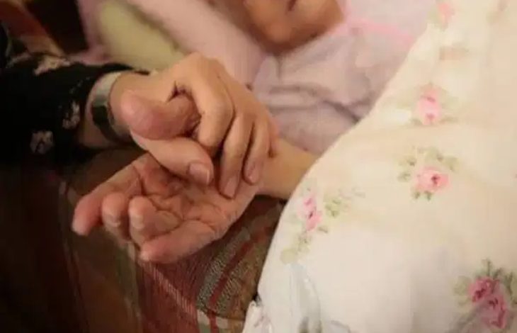 Görselde, yatakta uzanan yaşlı bir kişinin elini tutan başka bir kişi görülüyor. Yakın plandaki bu temas; bakım, destek ve duygusal dayanışma hissini öne çıkarırken, yaşlı bireylerin sosyal destek ihtiyacını çağrıştıran sakin ve içten bir anı yansıtıyor.