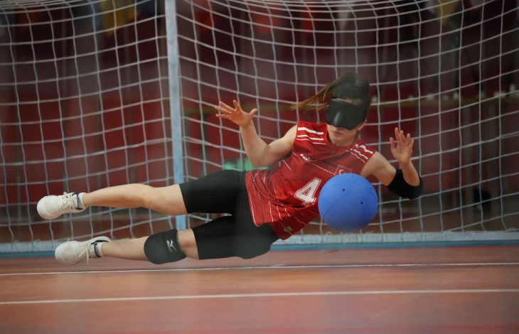 Kadın Goalball Milli Takımın dört numaralı sporcusu soluna yatarak topu kurtarıyor.