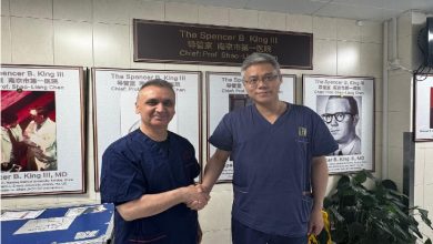 Fotoğrafta iki sağlık çalışanı veya doktor, hastane ortamında el sıkışırken görülüyor. Arkalarında tıbbi eğitim ve kardiyoloji alanıyla ilgili posterler yer alıyor. Görsel, uluslararası mesleki iş birliği, eğitim veya bilgi paylaşımını temsil eden resmi bir ziyaret anını yansıtıyor.