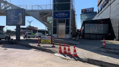 Yaya üst geçidinin yanında bulunan asansör kulesi önünde sürdürülen kaldırım ve yol çalışması görülüyor. Çalışma alanı trafik konileri ve uyarı levhalarıyla çevrilirken, bölgede erişilebilirlik düzenlemelerine yönelik çalışmalar dikkat çekiyor.