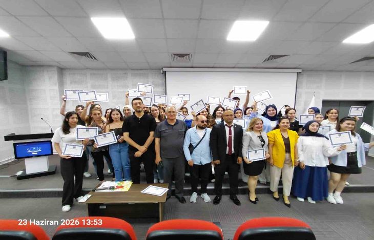 Bir konferans salonunda çekilen toplu fotoğrafta, çok sayıda genç ellerinde sertifikalarıyla poz veriyor. Ön sırada eğitmenler ve organizasyon temsilcileri yer alırken, katılımcılar başarılarını kutlayan neşeli bir görünüm sergiliyor. Görsel, eğitim programının tamamlanması sonrasında düzenlenen sertifika törenini yansıtıyor.