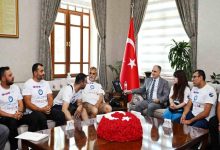 Resmî bir makam odasında gerçekleştirilen ziyarette, engelli sporcular ve proje temsilcileri bir araya gelmiş durumda. Türk bayrağının bulunduğu odada, takım tişörtleri giyen katılımcılar bir yetkiliyle görüşürken görülüyor. Görsel, engelli bireylerin yer aldığı bir spor veya sosyal sorumluluk projesine ilişkin resmî kabul ve destek sürecini yansıtıyor.