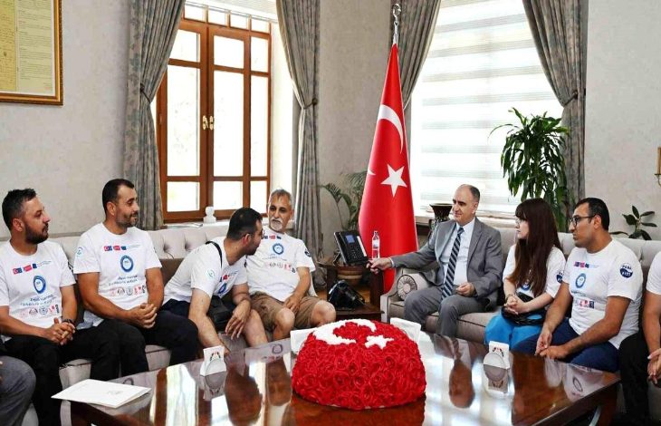 Resmî bir makam odasında gerçekleştirilen ziyarette, engelli sporcular ve proje temsilcileri bir araya gelmiş durumda. Türk bayrağının bulunduğu odada, takım tişörtleri giyen katılımcılar bir yetkiliyle görüşürken görülüyor. Görsel, engelli bireylerin yer aldığı bir spor veya sosyal sorumluluk projesine ilişkin resmî kabul ve destek sürecini yansıtıyor.