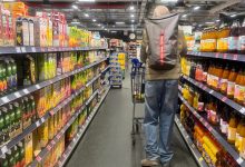 Bir süpermarket koridorunda alışveriş arabası kullanan bir kişi raflar arasında ilerliyor. Her iki tarafta içecek ve gıda ürünleri yer alırken, mağaza aydınlatması ve düzenli raflar dikkat çekiyor.