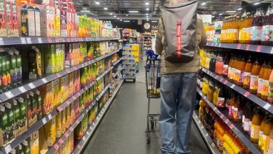 Bir süpermarket koridorunda alışveriş arabası kullanan bir kişi raflar arasında ilerliyor. Her iki tarafta içecek ve gıda ürünleri yer alırken, mağaza aydınlatması ve düzenli raflar dikkat çekiyor.