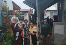 Görselde dar bir mahalle sokağında bir araya gelmiş beş kişi görülüyor. Bir kadın kucağında küçük bir çocuk taşırken, yanında iki çocuk ve bir başka kadın bulunuyor. Evlerin arasında çekilen fotoğraf samimi ve günlük yaşamdan bir kesit sunuyor. Görsel, aile ziyareti, sosyal destek veya toplumsal dayanışma amacıyla gerçekleştirilen bir buluşmayı yansıtıyor.