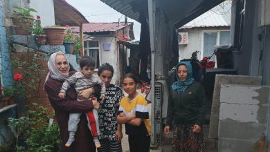 Görselde dar bir mahalle sokağında bir araya gelmiş beş kişi görülüyor. Bir kadın kucağında küçük bir çocuk taşırken, yanında iki çocuk ve bir başka kadın bulunuyor. Evlerin arasında çekilen fotoğraf samimi ve günlük yaşamdan bir kesit sunuyor. Görsel, aile ziyareti, sosyal destek veya toplumsal dayanışma amacıyla gerçekleştirilen bir buluşmayı yansıtıyor.