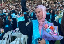 Serebral Palsili Öğrenci Büşra Gücük, mezuniyet cübbesi giyili, elinde kep ve kucağında çiçek tutarak poz veriyor.