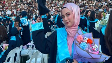 Serebral Palsili Öğrenci Büşra Gücük, mezuniyet cübbesi giyili, elinde kep ve kucağında çiçek tutarak poz veriyor.