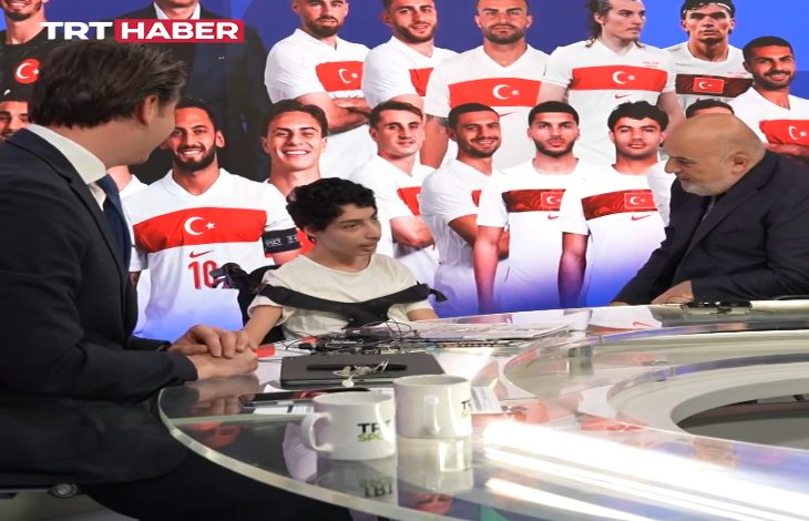 Bir televizyon stüdyosunda gerçekleşen yayında, genç bir çocuk masada sunucularla sohbet ediyor. Arka planda Türkiye forması giymiş sporcuların büyük görselleri yer alırken, TRT Haber logosu ekranda görünüyor. Spor odaklı sıcak ve samimi bir yayın anı yansıtılıyor.