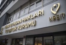 Görselde, Türkiye İnsan Hakları ve Eşitlik Kurumu'nun (TİHEK) hizmet binasının dış cephesi ve giriş kısmı yer almaktadır. Beyaz bir zemin üzerine, kabartmalı ve altın sarısı renkte büyük harflerle "TÜRKİYE İNSAN HAKLARI VE EŞİTLİK KURUMU" yazmaktadır. Bu yazının sağ tarafında kurumun amblemi ve altında İngilizce kısaltması olan "HREIT" ibaresi bulunur. Sol alt köşede ise kurumun küçük bir logosu yer almaktadır. Binanın girişinde camekanlı kapılar ve üst katlara ait pencereler görünmektedir.