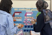 İki kişi renkli bir eğitim panosu önünde duruyor, kâğıt balıklarla etkileşimli bir çalışma yapıyor.