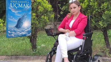 Tekerlekli sandalyesinde oturan genç bir kadın, açık havada yeşillikler arasında poz veriyor. Üzerinde parlak pembe bir blazer, beyaz pantolon ve beyaz ayakkabılar var; güneş gözlüğü başının üzerinde duruyor. Sol tarafta mavi tonlarda bir kitap kapağı yer alıyor: Kırık Kanatla Uçmak. Kapakta bulutlar arasında ışığa doğru yükselen kanatlı bir figür görülüyor.