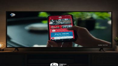 Televizyon ekranında, elde tutulan bir akıllı telefonda Türkiye Milli Paralimpik Komitesi’nin mobil uygulaması görüntüleniyor. Ekranda Paris 2024 içerikleri yer alırken, altta TMPK logosu bulunuyor.
