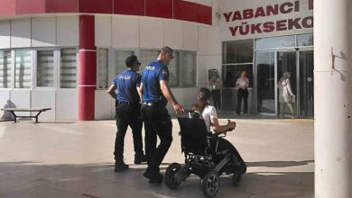 Görselde bir yükseköğretim kurumu girişinde iki polis memuru, tekerlekli sandalyedeki bir öğrenciye eşlik ediyor. Öğrenci bina girişine doğru yönlendirilirken arka planda sınav merkezi atmosferi görülüyor. Kare, erişilebilirlik ve destek anını yansıtıyor.