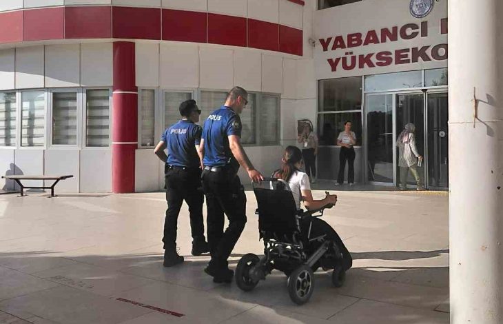 Görselde bir yükseköğretim kurumu girişinde iki polis memuru, tekerlekli sandalyedeki bir öğrenciye eşlik ediyor. Öğrenci bina girişine doğru yönlendirilirken arka planda sınav merkezi atmosferi görülüyor. Kare, erişilebilirlik ve destek anını yansıtıyor.