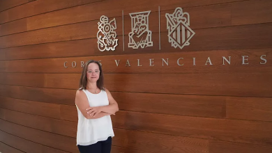 Down sendromlu Mar Galcerán, ahşap kaplamalı bir duvar önünde ayakta poz veriyor. Arkasında Valencia Bölge Parlamentosu'nun "Corts Valencianes" yazısı ve resmi amblemleri yer alıyor. Görsel, Galcerán'ın İspanya'da parlamentoya girerek tarihe geçtiği haberi temsil ediyor.