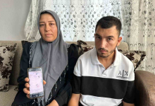 Bir kadın ve genç bir erkek ev ortamında yan yana oturuyor. Kadın elindeki cep telefonunda resmi bir belgeyi gösterirken, ikisi de kameraya bakıyor. Görsel, doğuştan engelli Hasan'a 20 yıl sonra "engelli değildir" raporu verilmesine ilişkin haberi temsil ediyor.