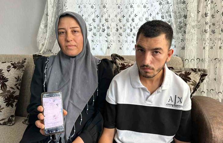 Bir kadın ve genç bir erkek ev ortamında yan yana oturuyor. Kadın elindeki cep telefonunda resmi bir belgeyi gösterirken, ikisi de kameraya bakıyor. Görsel, doğuştan engelli Hasan'a 20 yıl sonra "engelli değildir" raporu verilmesine ilişkin haberi temsil ediyor.