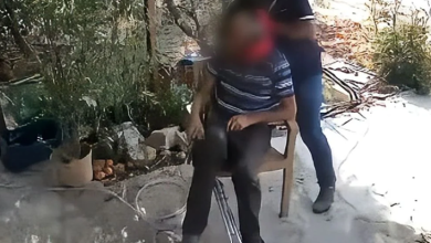 Açık alanda sandalyede oturan ortopedik engelli bir bireyin yanında, yüzü bulanıklaştırılmış iki kişi görülüyor. Görüntü, olayla ilgili güvenlik kamerası veya kayıt görüntüsünden alınmış.