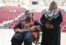 Abdulsamet Sert, mezuniyet cübbesi giyinmiş olarak tekerlekli sandalyede bulunuyor ve annesi yanında ayakta durmakta.