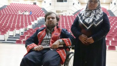 Abdulsamet Sert, mezuniyet cübbesi giyinmiş olarak tekerlekli sandalyede bulunuyor ve annesi yanında ayakta durmakta.