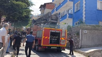 Görselde, dar bir sokakta park halinde bulunan bir itfaiye aracı ile çevresinde toplanan itfaiye ekipleri, polisler ve vatandaşlar görülüyor. Yol kenarındaki apartmanların önünde müdahale hazırlıkları sürerken, olay yerine güvenlik ve acil durum ekiplerinin sevk edildiği an yansıyor.