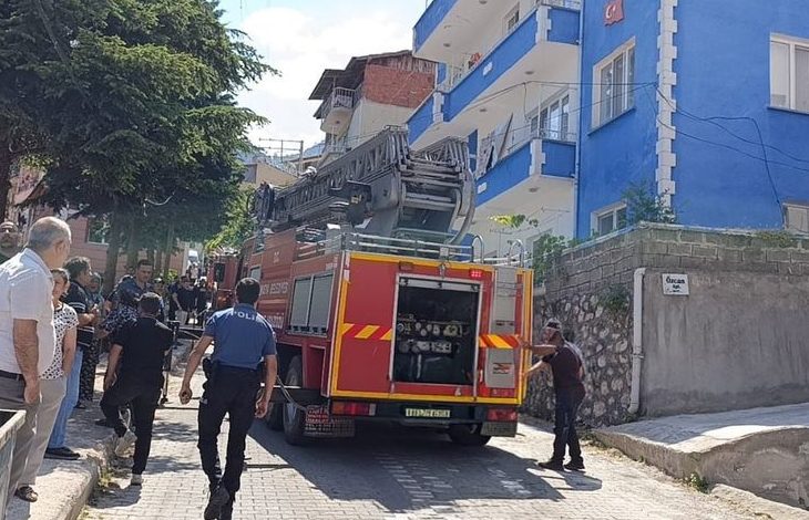 Görselde, dar bir sokakta park halinde bulunan bir itfaiye aracı ile çevresinde toplanan itfaiye ekipleri, polisler ve vatandaşlar görülüyor. Yol kenarındaki apartmanların önünde müdahale hazırlıkları sürerken, olay yerine güvenlik ve acil durum ekiplerinin sevk edildiği an yansıyor.
