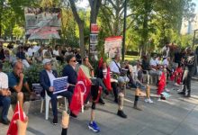 Parkta toplanan gaziler, ellerinde Türk bayrakları ve çeşitli pankartlarla oturarak bir protesto etkinliğine katılıyor; bazı katılımcıların protez bacak kullandığı da görülüyor.