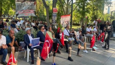 Parkta toplanan gaziler, ellerinde Türk bayrakları ve çeşitli pankartlarla oturarak bir protesto etkinliğine katılıyor; bazı katılımcıların protez bacak kullandığı da görülüyor.